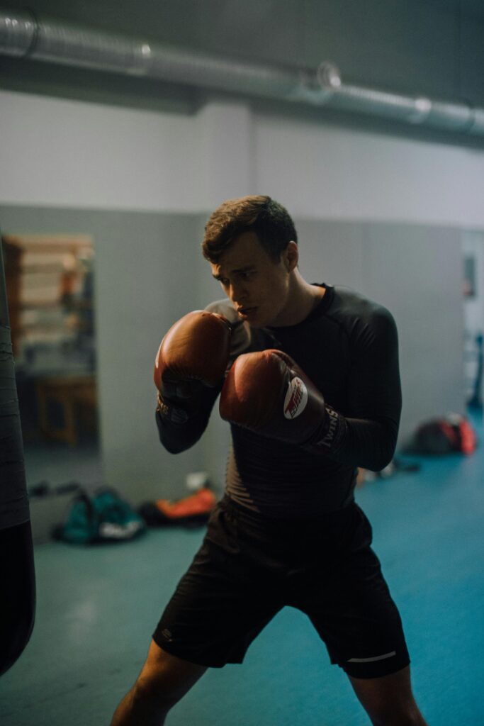 Focused male athlete boxing in a gym setting, practicing punches with gloves.
